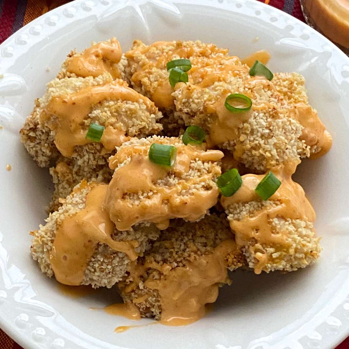 Healthy, baked bang bang chicken drizzled with bang bang sauce in a bowl and topped with sliced green onion.