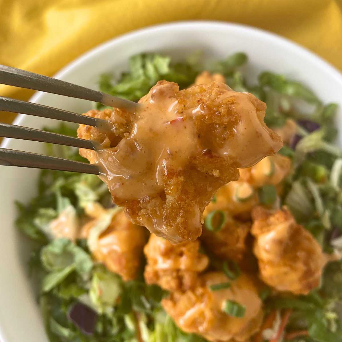 Fork holding a chicken nugget coated with bang bang sauce.