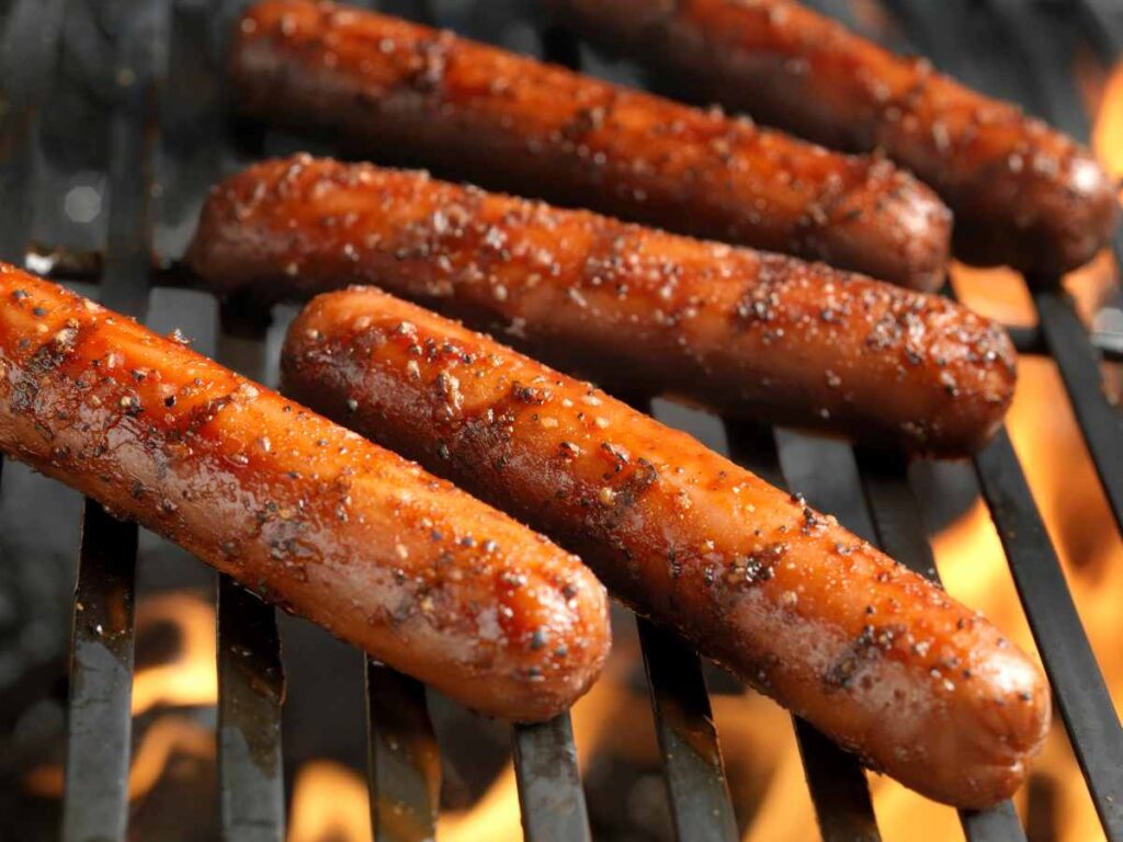 Five grilled hot dogs on a grill grate.