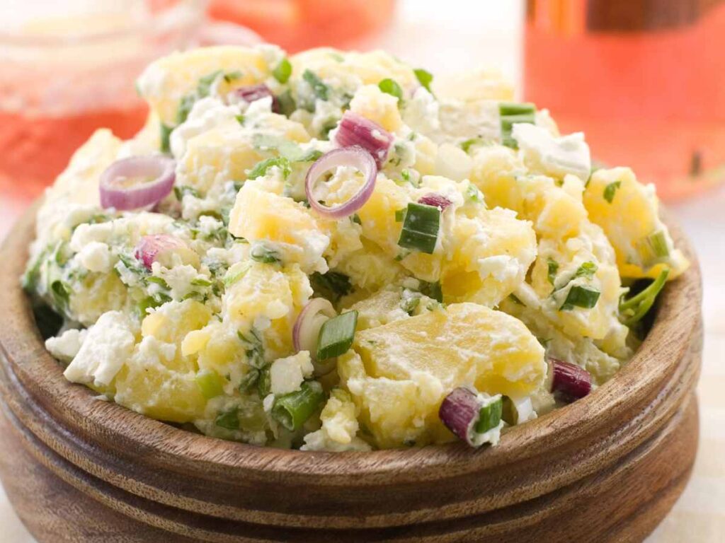 Creamy potato salad garnished with red onions an scallions in a brown bowl.