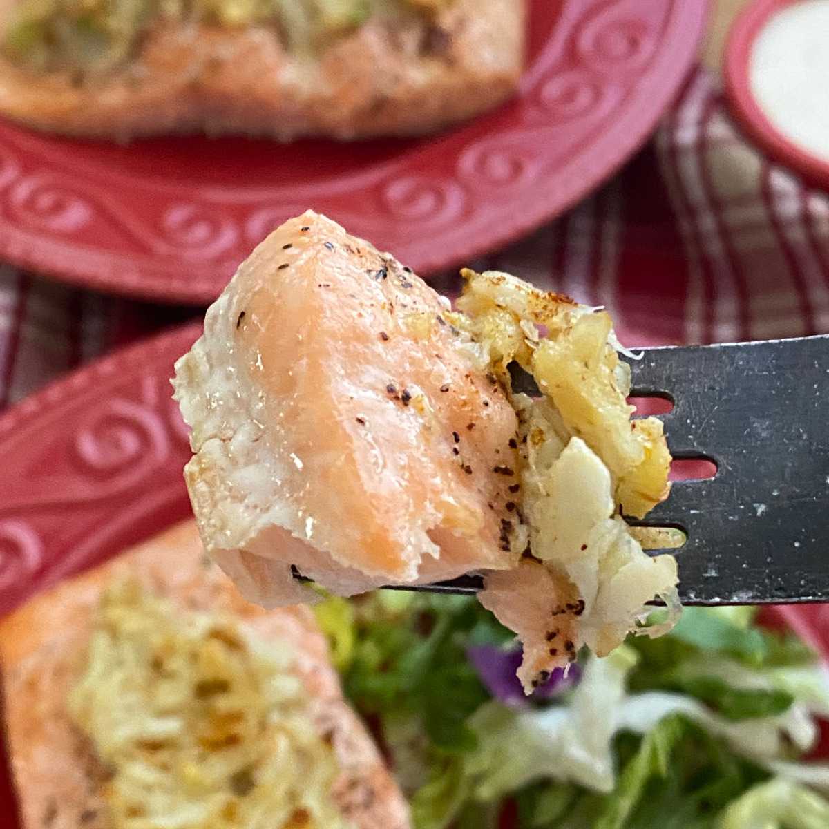 Fork holding a bite of salmon stuffed with crab over a plate with the rest of the fish.