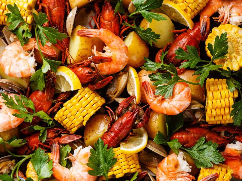 Shrimp, fish, corn on the cob, and parsley from a seafood boil spread out on a platter.