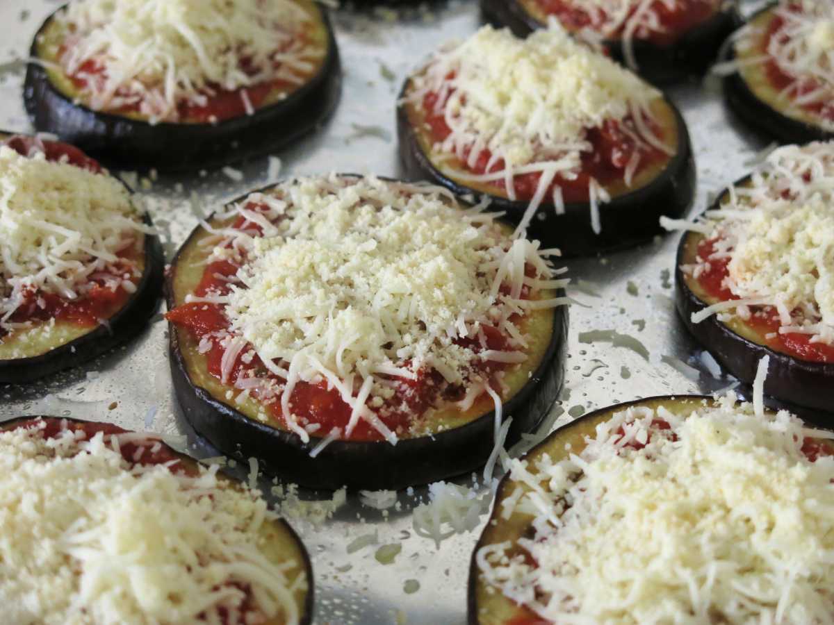 Eggplant parmesan rounds topped with marinara, mozzarella, and Parmesan cheese before cooking.