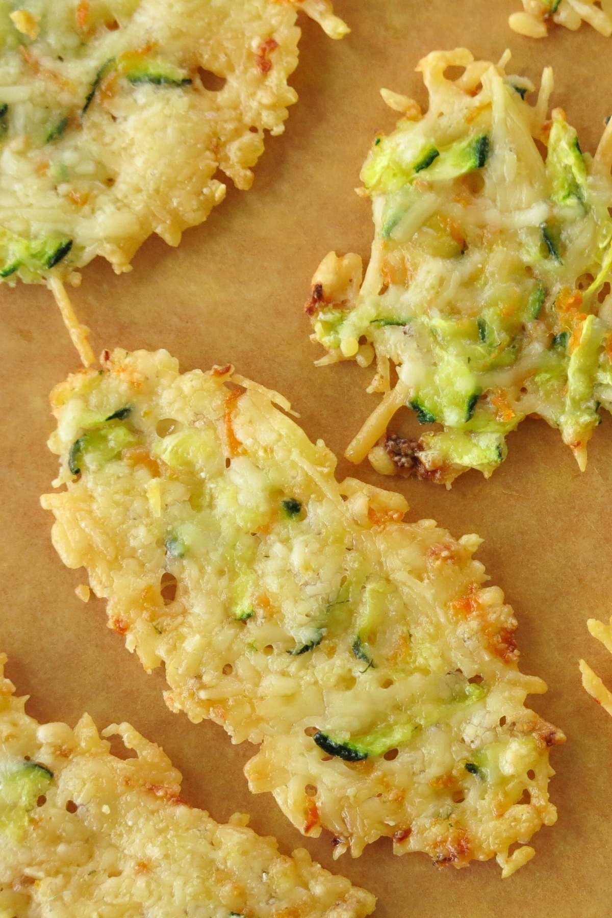 Parmesan crisps baked in the oven with shreds of zucchini and carrot with one that looks like it is smiling.