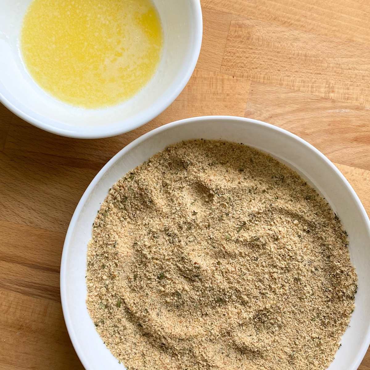 Melted butter in a small bowl and a shallow plate with parmesan breading.