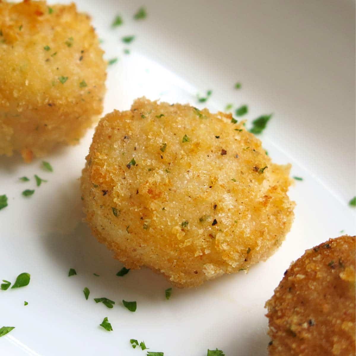 Parmesan Crusted Broiled Scallops lined up on a plate with minced parsley around them.
