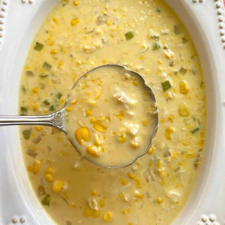 Ladle lifting creamy crab corn soup out of a serving bowl.