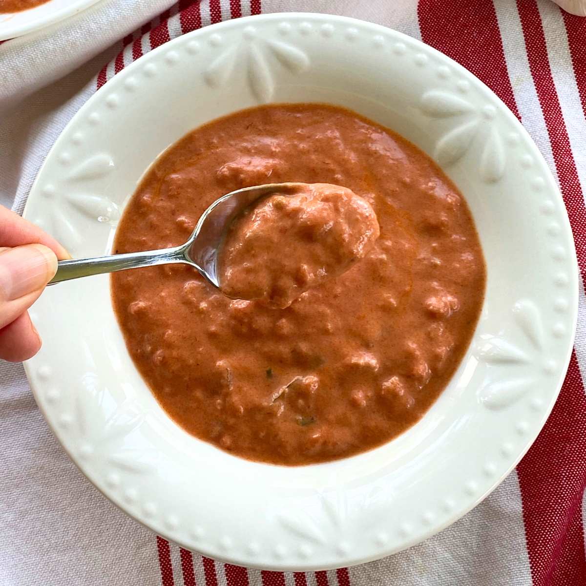 Spoon holding lobster ravioli sauce over a white bowl with more sauce.