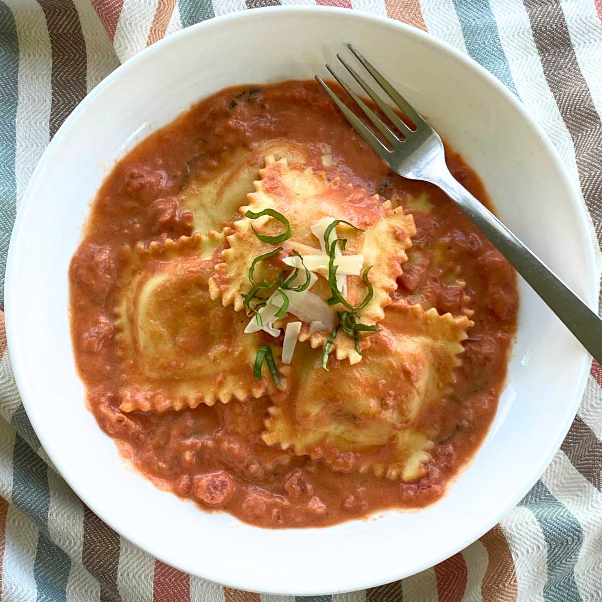 Easy lobster ravioli sauce in bowl topped with lobster ravioli, parmesan cheese, and strips of fresh basil.