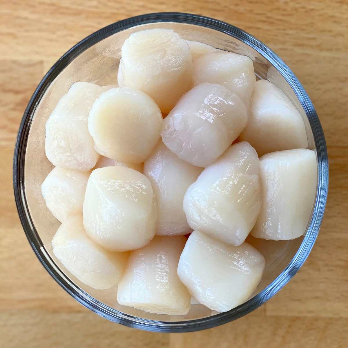 Glass bowl with large uncooked sea scallops in it.
