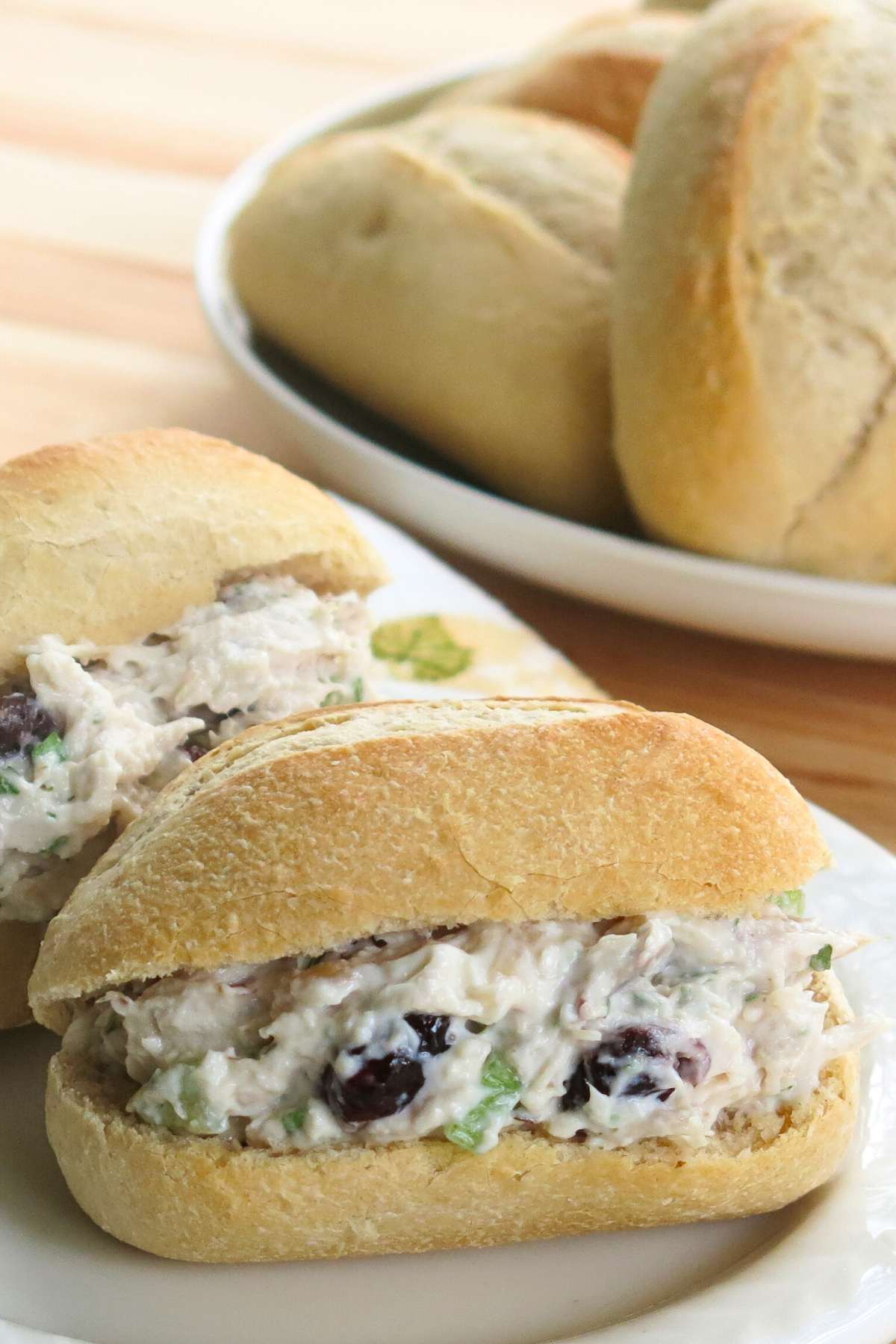 Creamy chicken salad made with leftover shredded chicken inside two small oblong rolls on a plate.. 