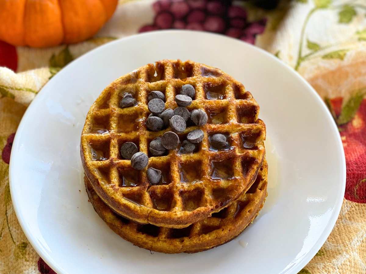 Two pumpkin chaffles topped with chocolate chips on a white plate.
