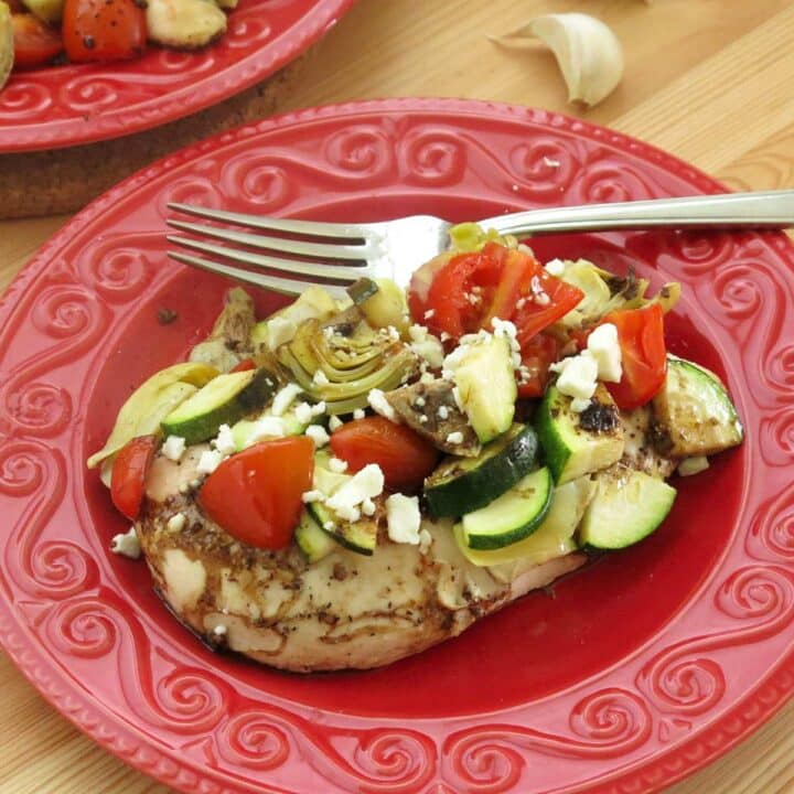 A serving of Mediterranean chicken bake with zucchini, artichokes, tomatoes, and a balsamic vinaigrette on a plate with a fork.