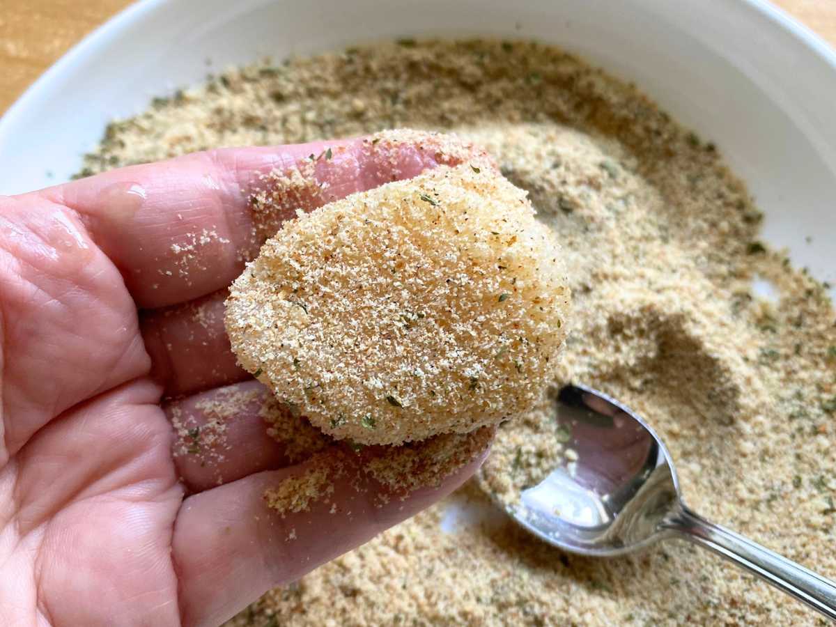 Hand holding a sea scallop lightly covered with Parmesan breading.