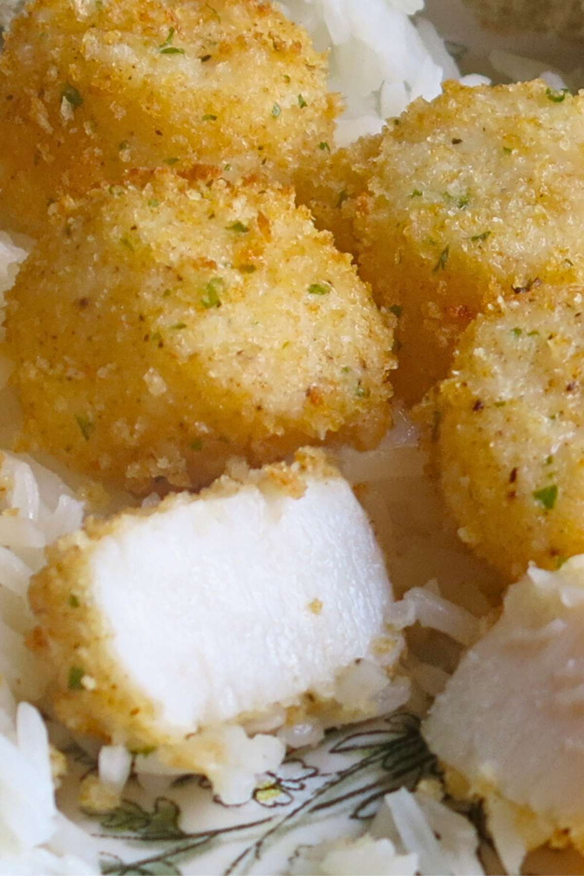 Broiled scallops with Parmesan breading on a plate over rice with one cut in half to expose the moist, white center.