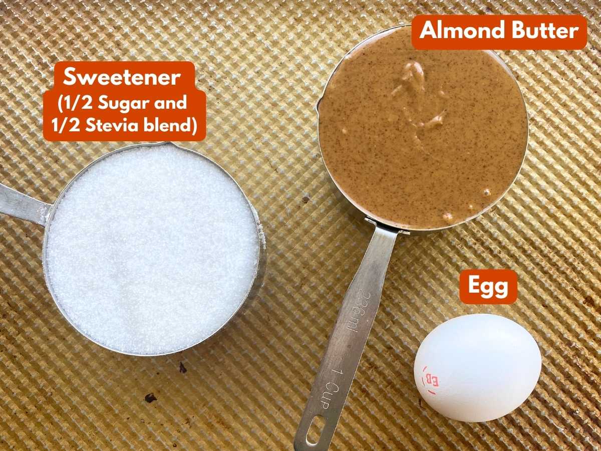 Ingredients in measuring cups to make almond butter cookies: almond butter, sugar and stevia blend, and an egg.