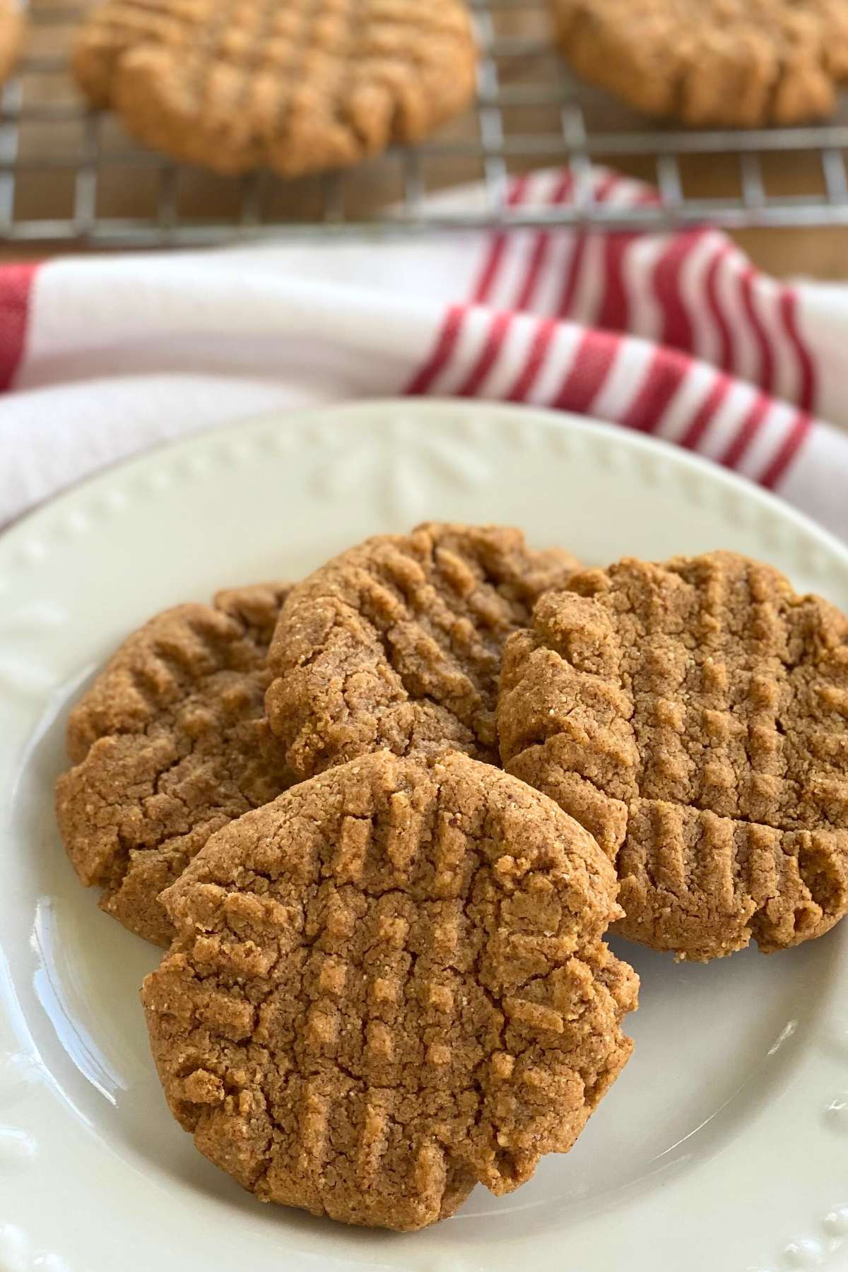 Gluten-free almond butter cookies on a plate with more on a cooling rack behend it.