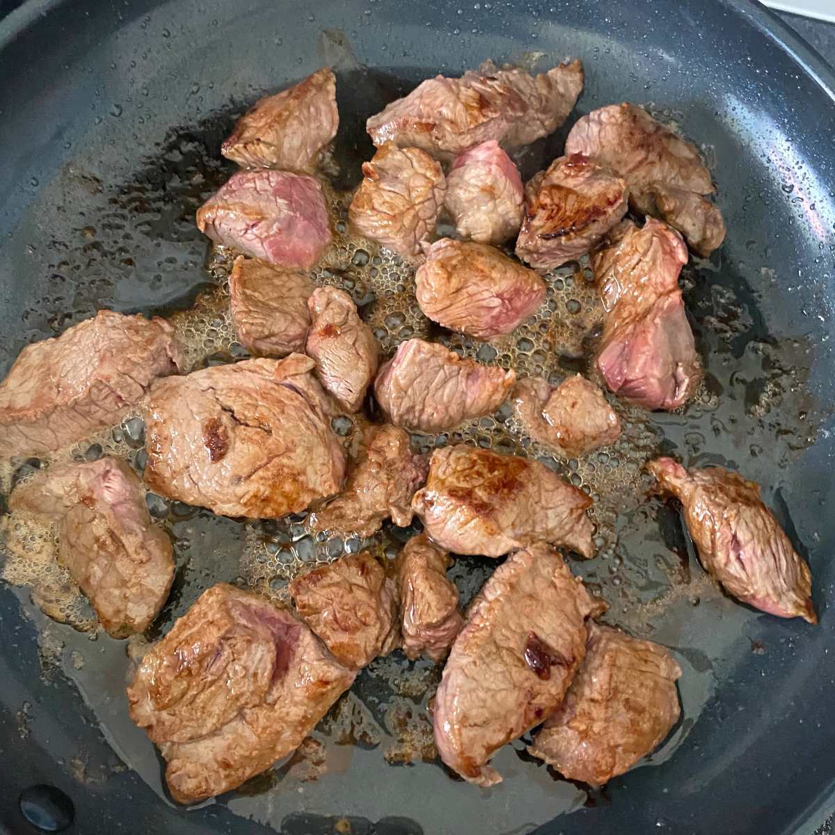 Partially browned cubes of beef chuck roast in a large skillet.