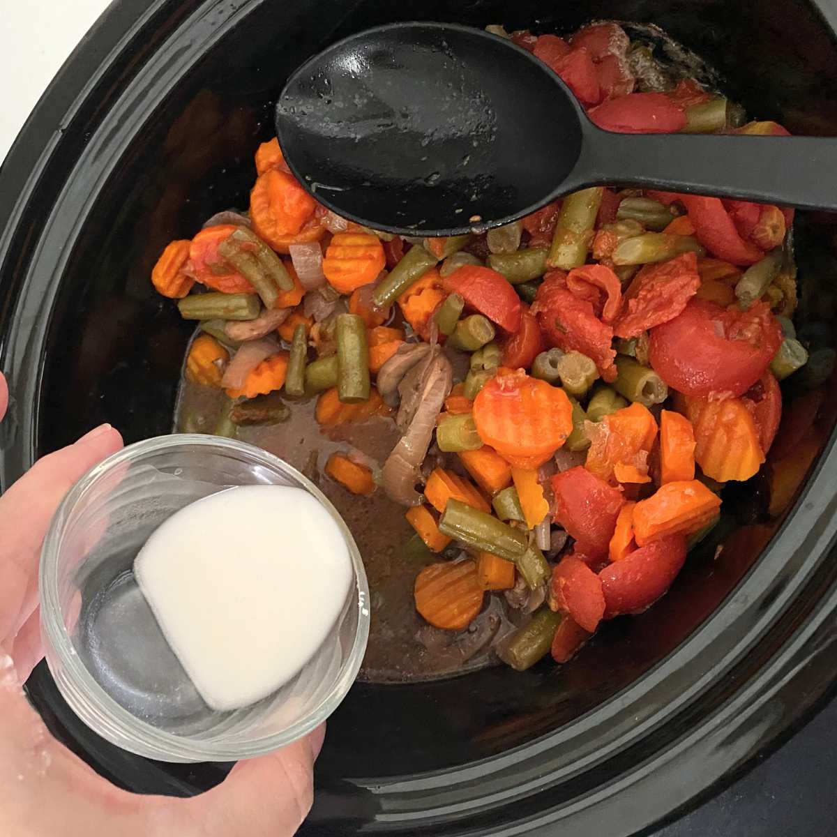 Cornstarch water slush being poured into crock with cooked beef and vegetable stew.