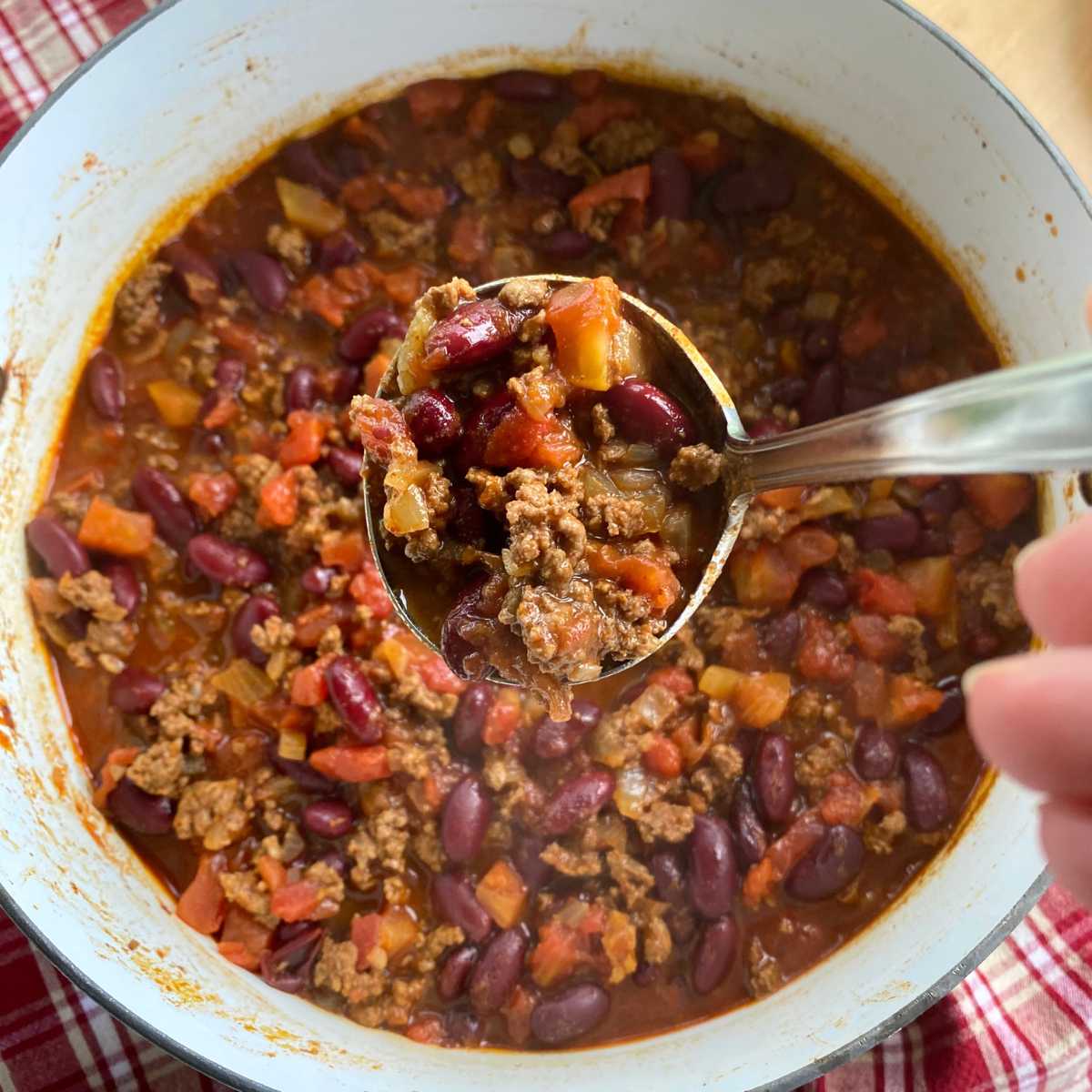 Ladle lifing out beef and bean chili out of a large stock pot.