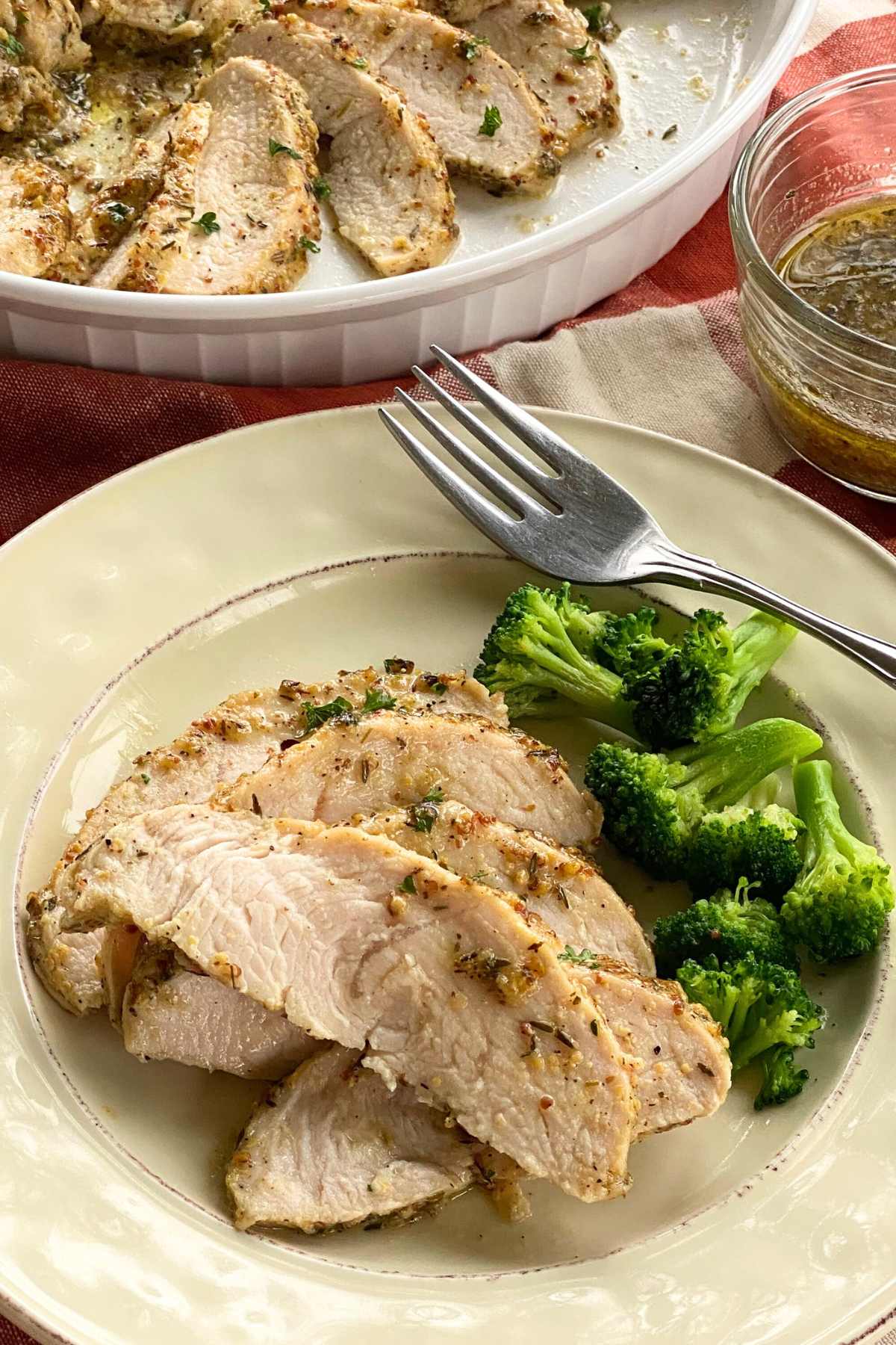 Plate with five slices of baked turkey tenderloin next to broccoli with a platter of more behind it.