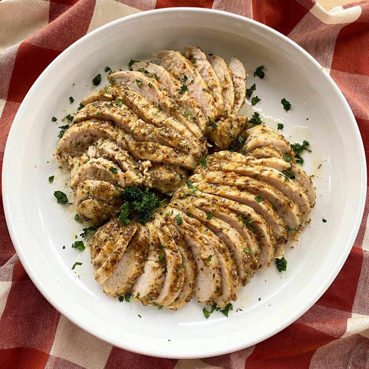 Sliced turkey tenderloin marinated in a maple, dijon mustard, garlic mixture on a large round white platter garnished with parsley.