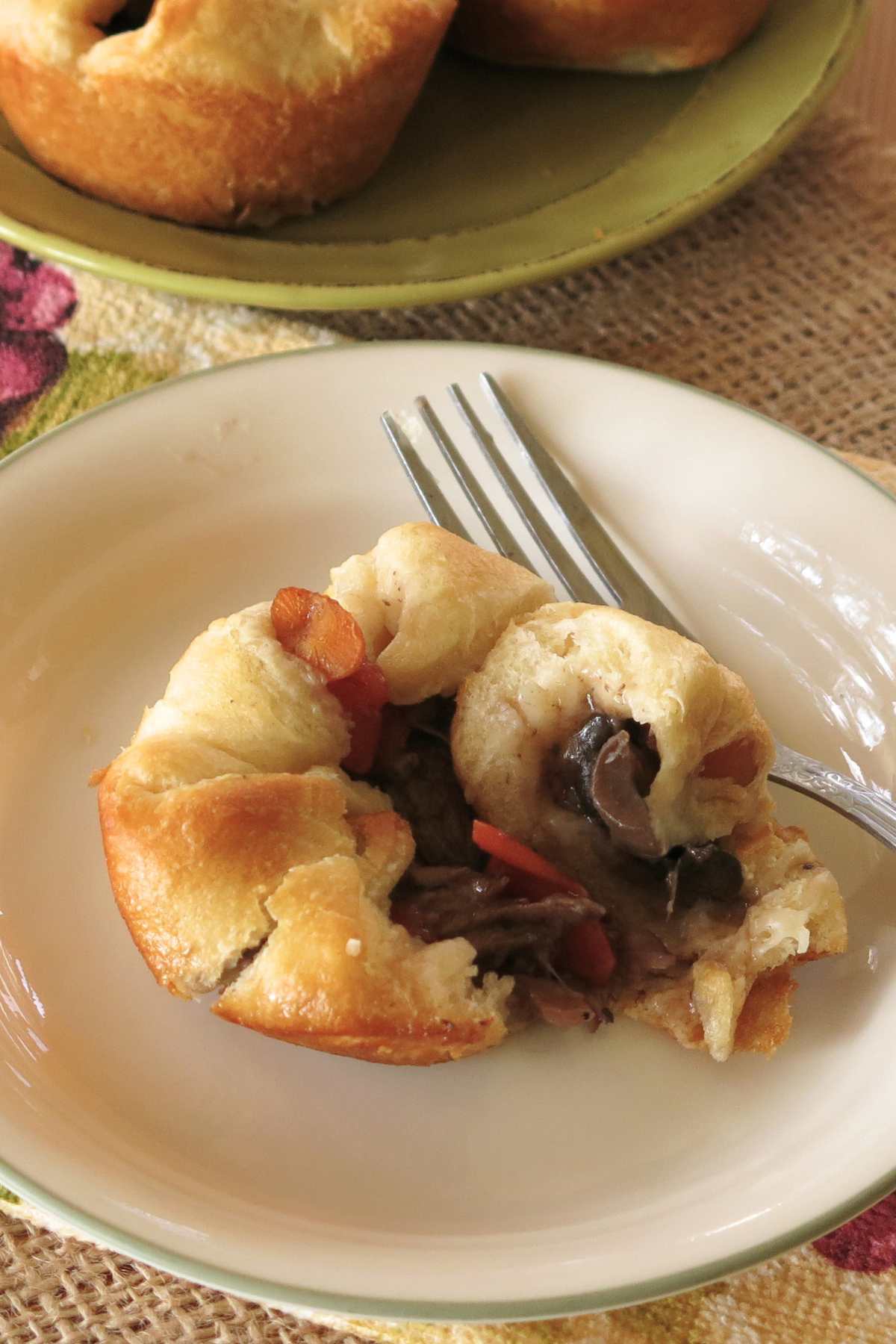 Individual beef crescent roll pot pie opend up on a plate with a fork