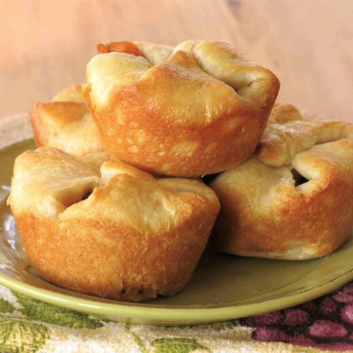 Four beef crescent roll pot pies baked in a muffin tin stacked on a plate.