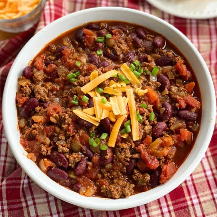 Large bowl of homemade Southern chili with beef in beans in a serving bowl and topped with shredded cheddar cheese and sliced green onions.