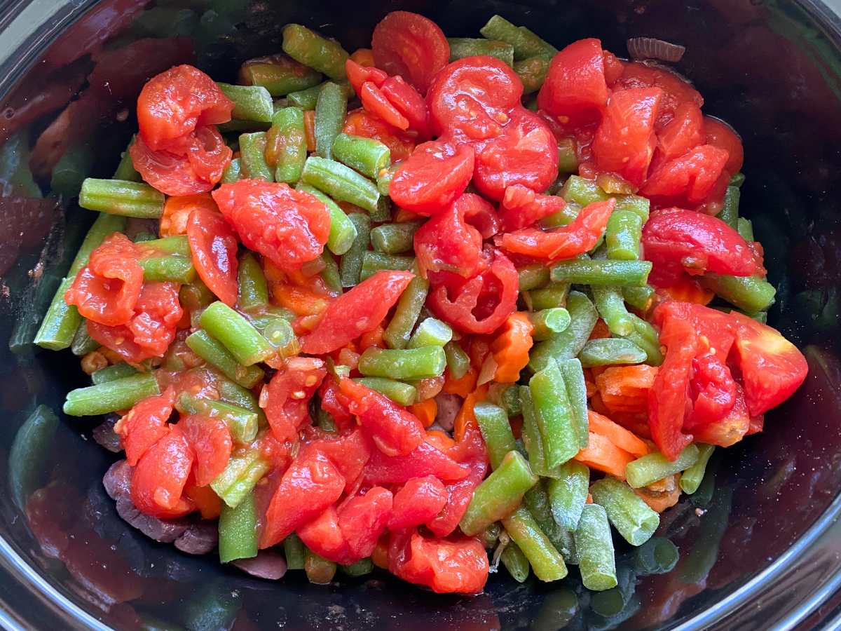 All ingredients in slow cooker with stewed tomatoes, frozen green beans, and frozen carrots showing.