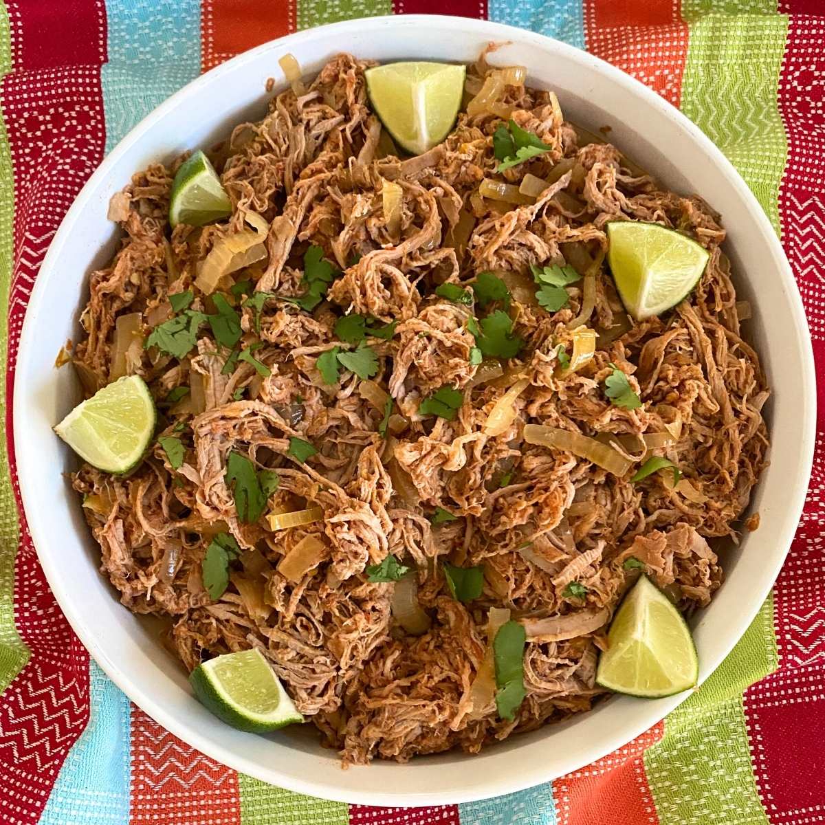 Salsa pork tenderloin carnitas in a round platter with lime wedges and cilantro.