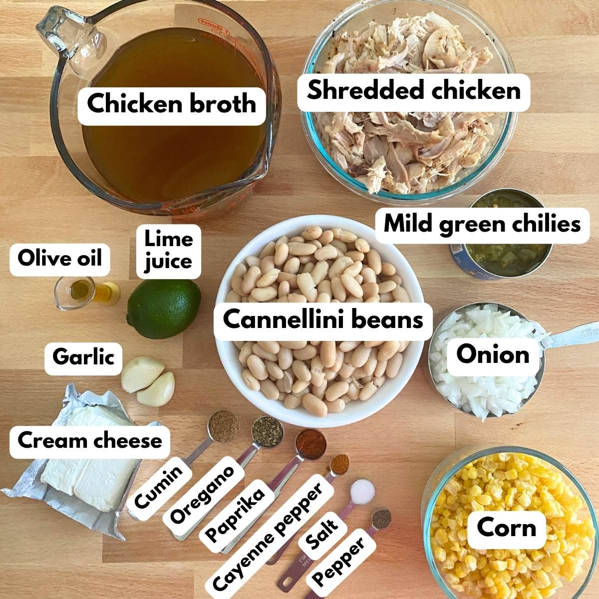 Labeled ingredients to make white chicken chili: Broth, shredded chicken, cannellini beans, diced green chiles, cream cheese, onion, corn, spices, lime juice, garlic, and olive oil.