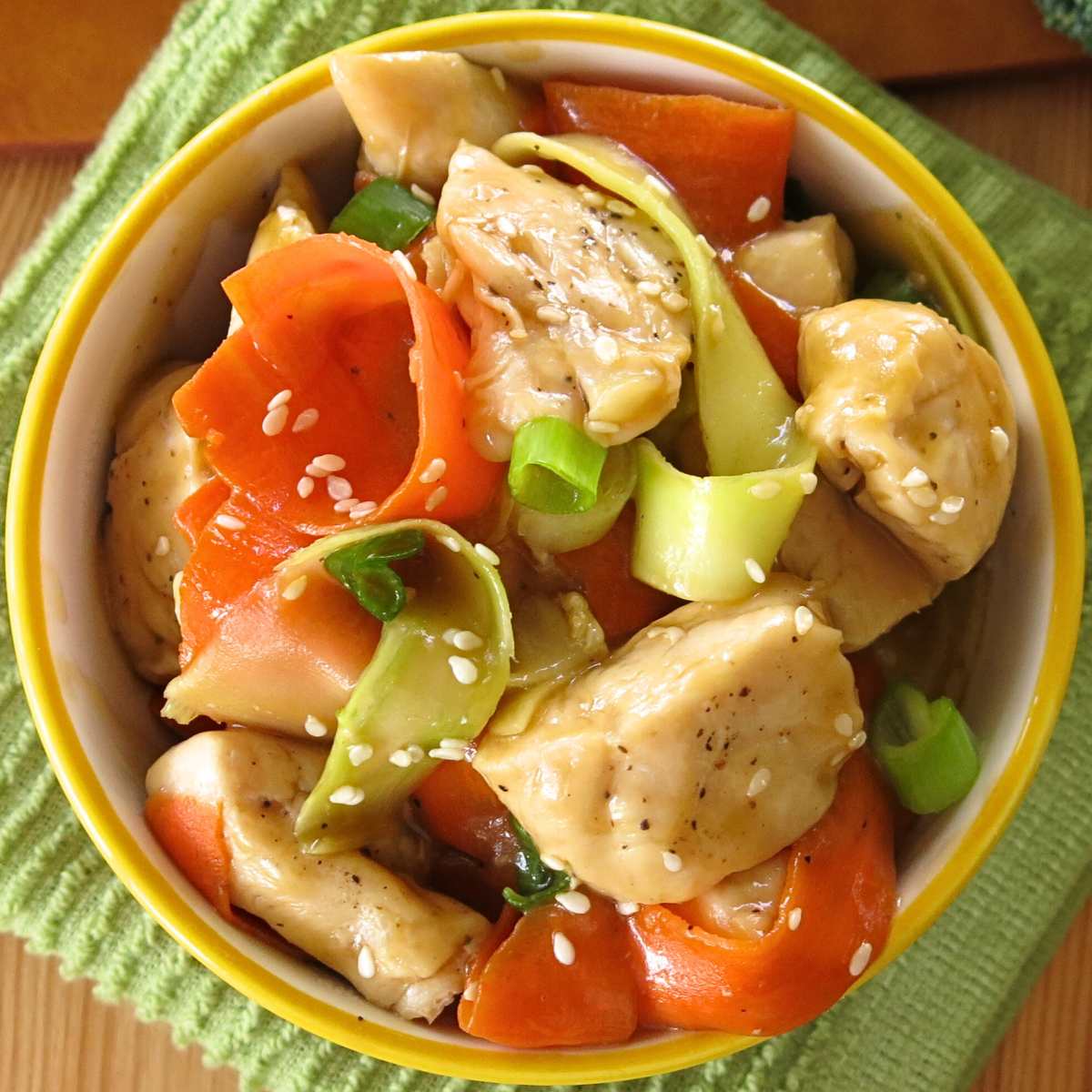 Healthy spicy orange chicken in a bowl with ribbons of carrot and broccoli.