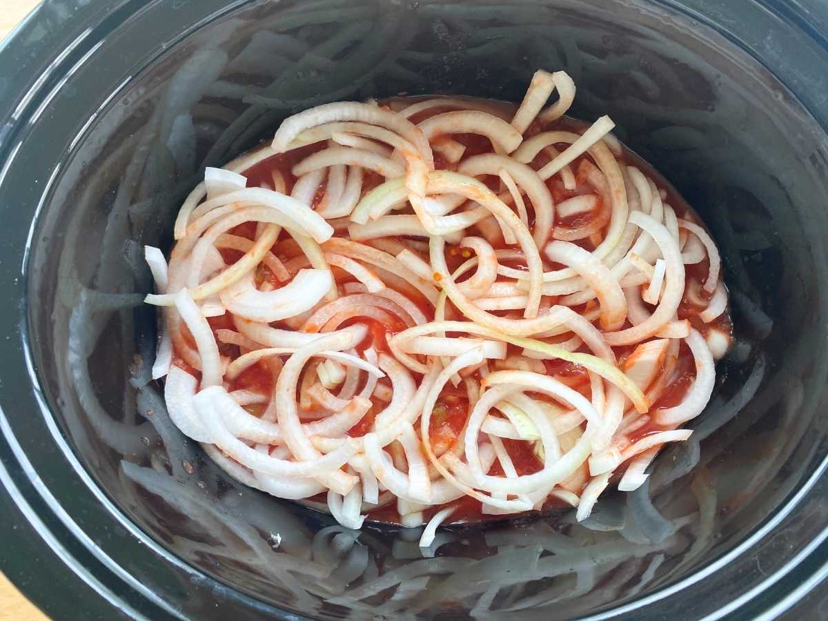 Slow cooker with uncooked pork tenderloin, salsa, and onions layered inside.