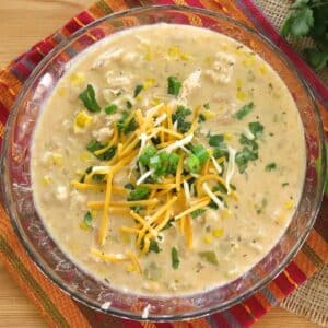 Creamy white chicken chili made with cream cheese in a glass bowl topped with cilantro, green onions, and shredded cheese.
