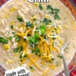 White chicken chili made with cream cheese in a glass bowl with a spoon.