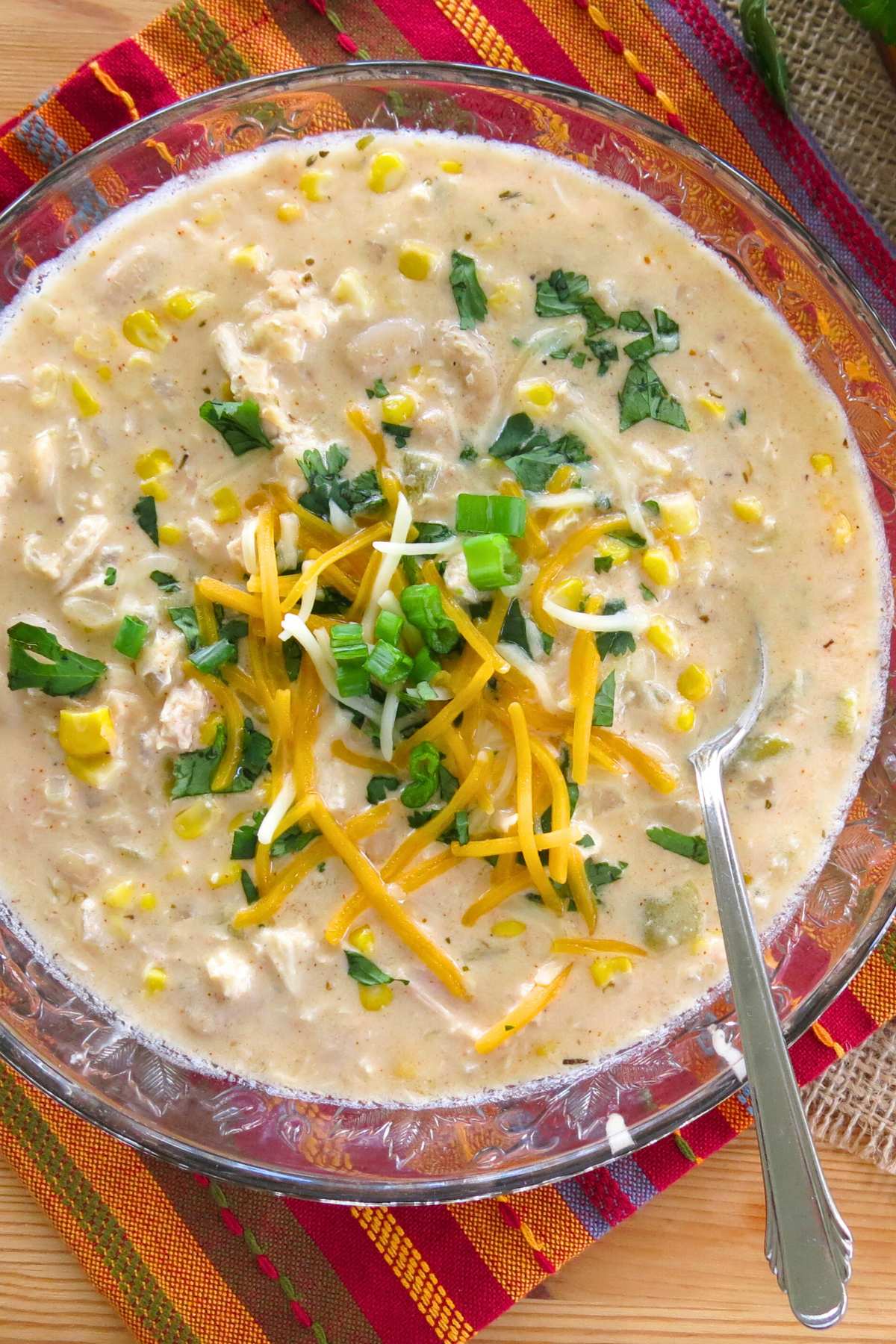 Bowl of white chicken chili topped with shredded cheese, sliced green onions, and cilantro.