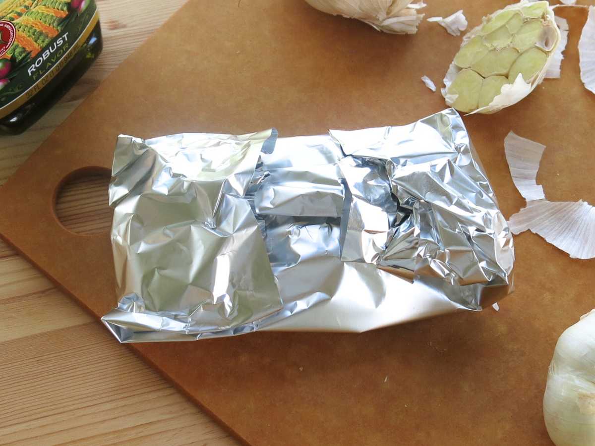 Prepped head of garlic in aluminum foil packet with sliced top outside the packet.