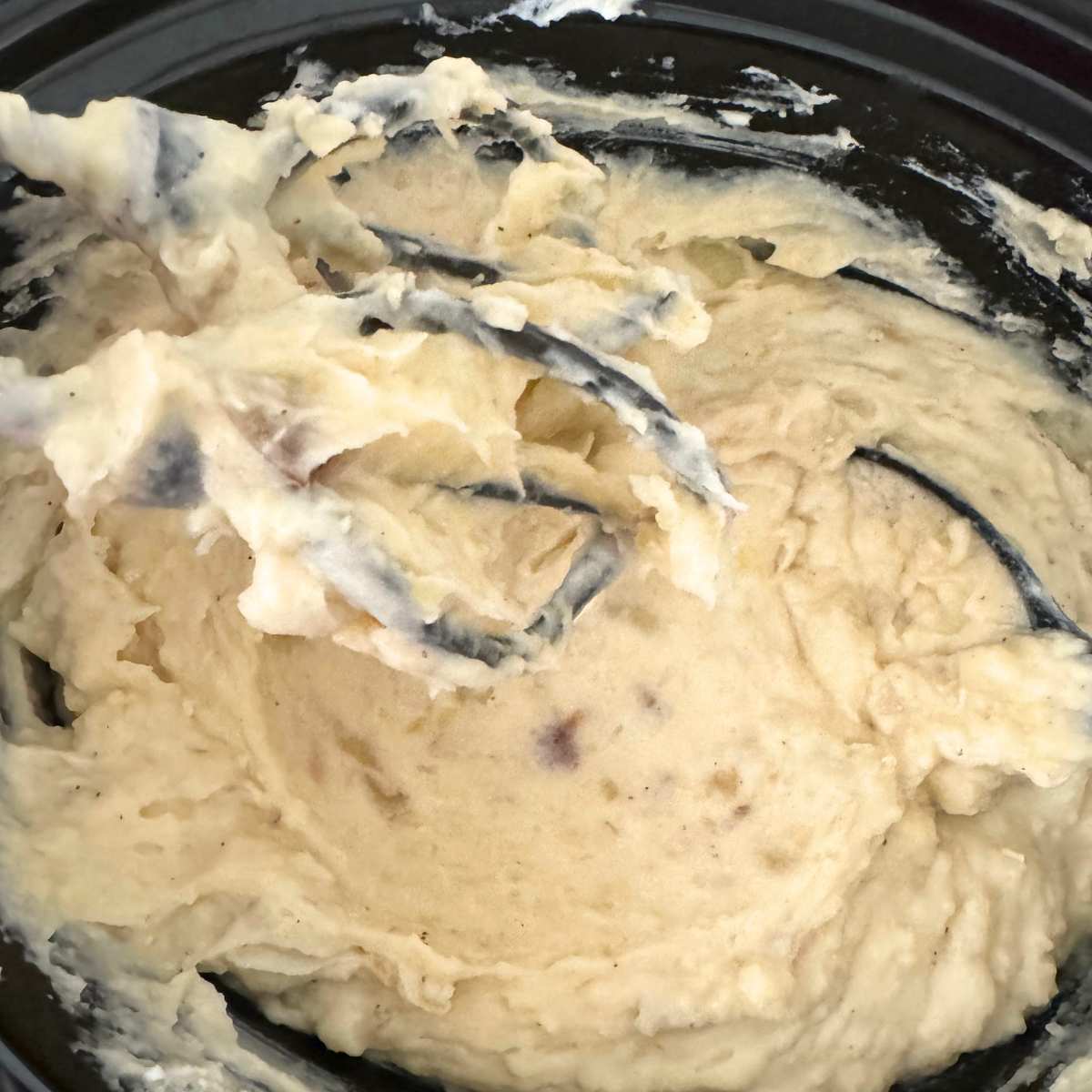 Electric beaters inside the crockpot with creamy mashed potatoes.