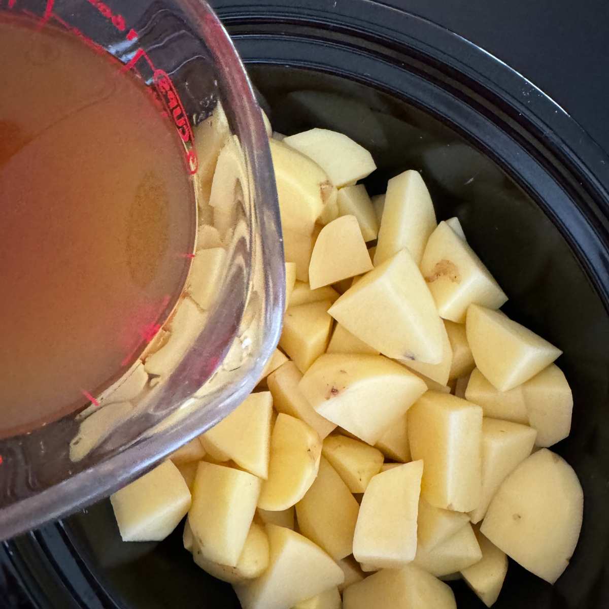 Peeled and chopped Yukon gold potatoes in a crock-pot with vegetable broth being poured over the top.