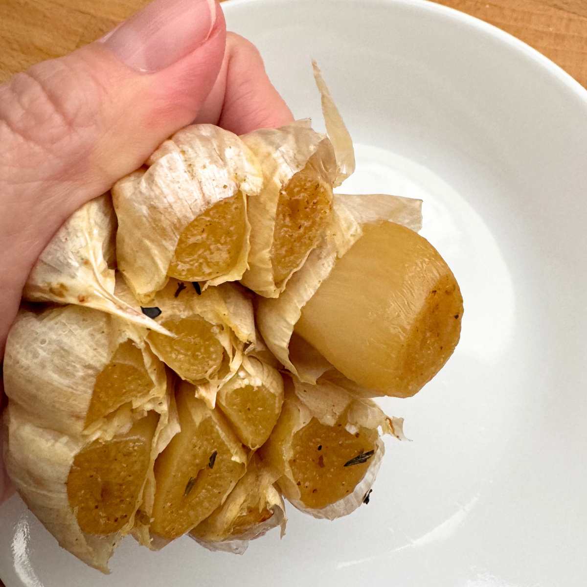 Hand squeezing garlic of garlic with a clove coming out.