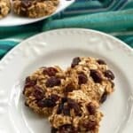 Three healthy banana oatmeal raisin cookies on a plate with more on a platter behind it.