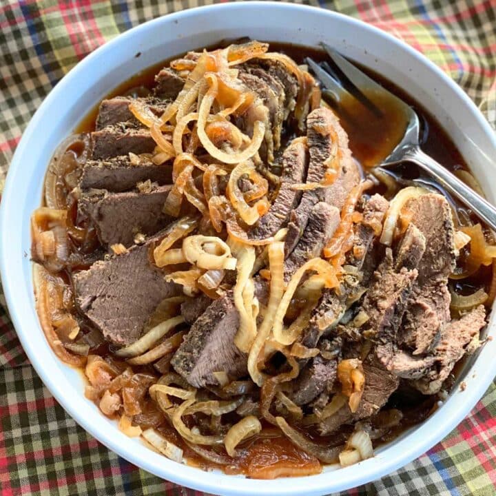 Sliced crock-pot bottom round roast on platter surrounded by cooked onions and beef consomme.