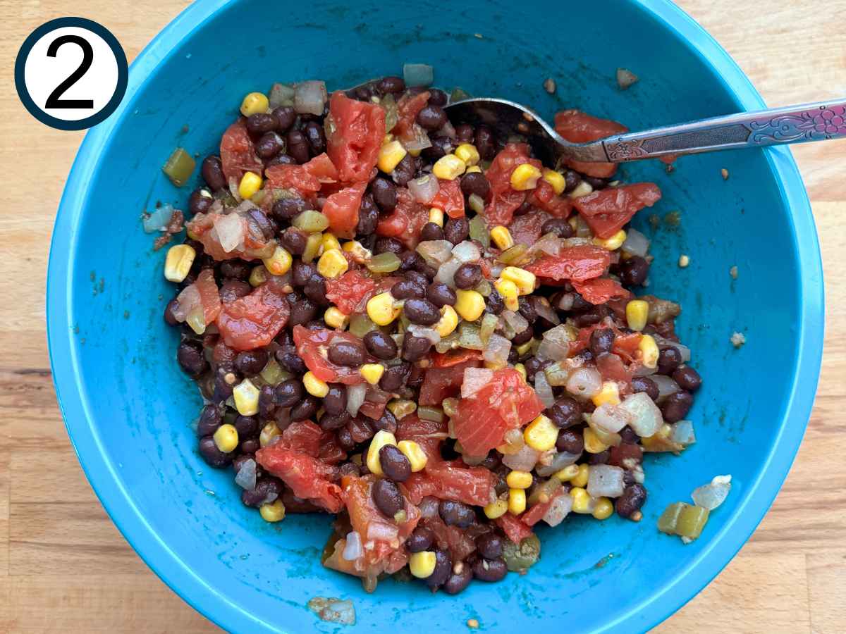 Black beans, corn, tomatoes, peppers, garlic, olive oil, lime, juice, and spices mixed together into a turquoise bowl.