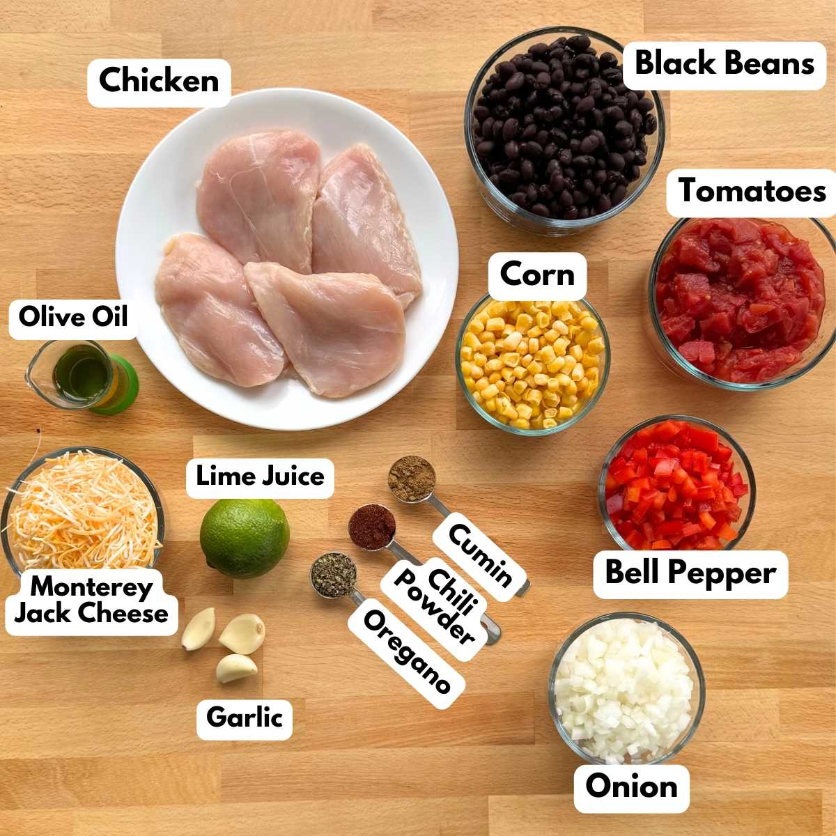 Labeled ingredients to make cowboy chicken recipe: chicken, black beans, corn, tomatoes, bell pepper, onion, shredded cheese, cumin, chili powder, oregano, lime, garlic, lime juice.