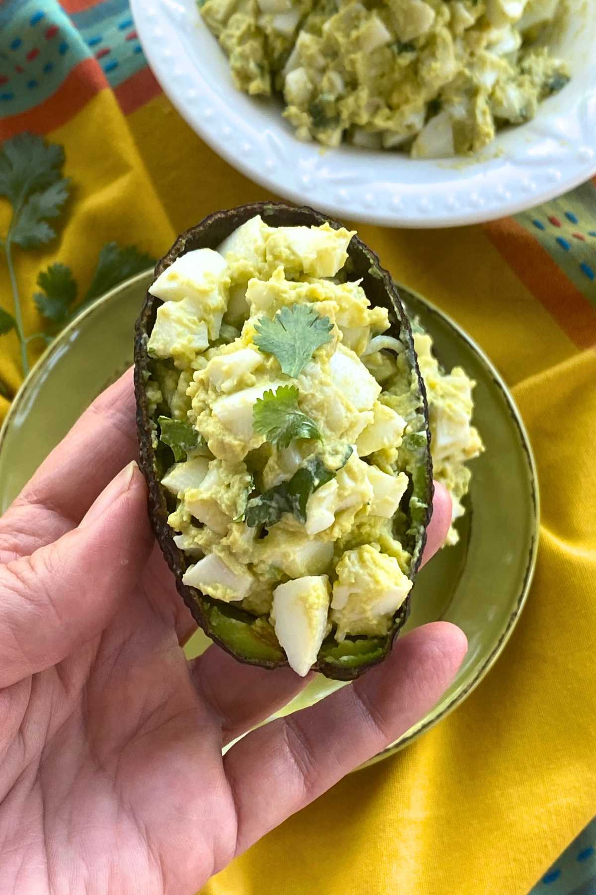 Hand holding a scooped out avocado half filled with healthy egg salad.