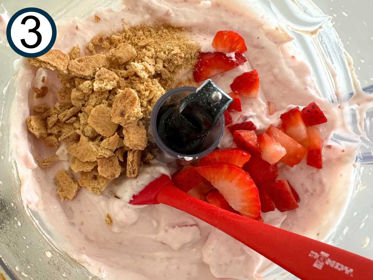 Crumbled graham crackers and chopped strawberries being mixed into creamy cottage cheese base.