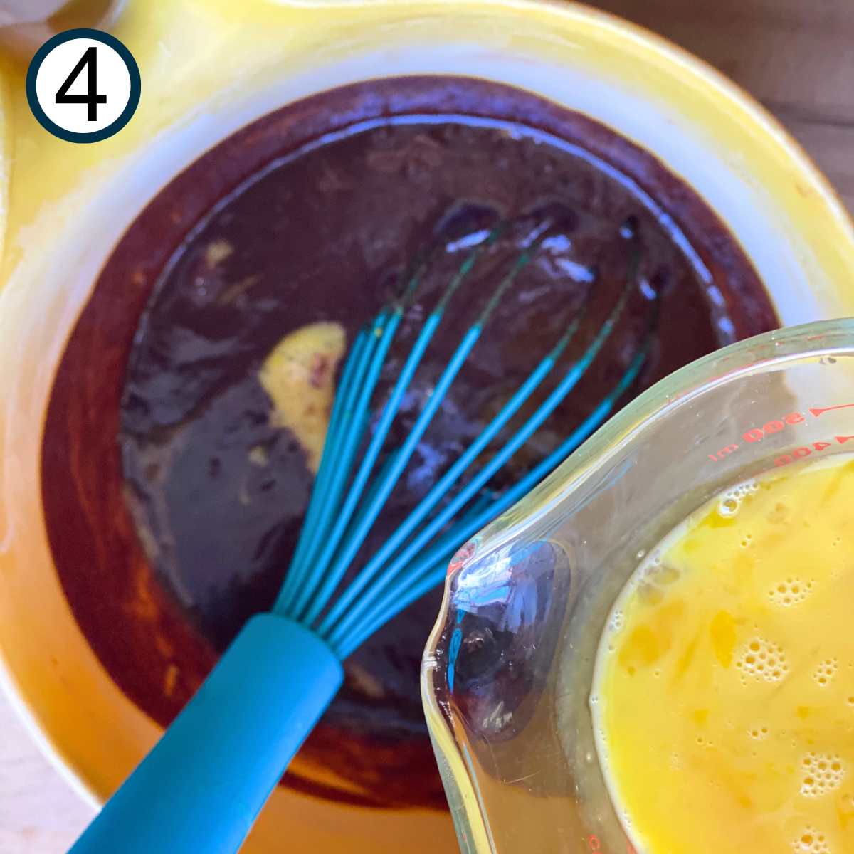 Whisked eggs being poured in the chocolate and butter mixture for flourless chocolate cake.