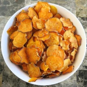 Baked sweet potato chips in a large white bowl on a marble table.