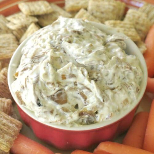 Caramelized onion dip with Greek yogurt in a bowl surrounded by carrots and crackers.